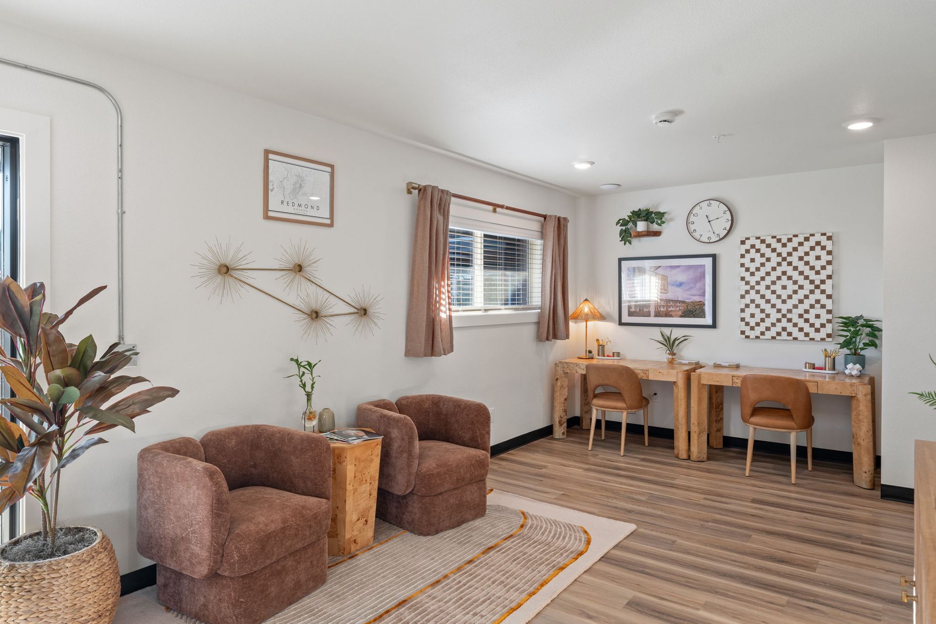 A living room with two chairs , a desk and a clock on the wall.