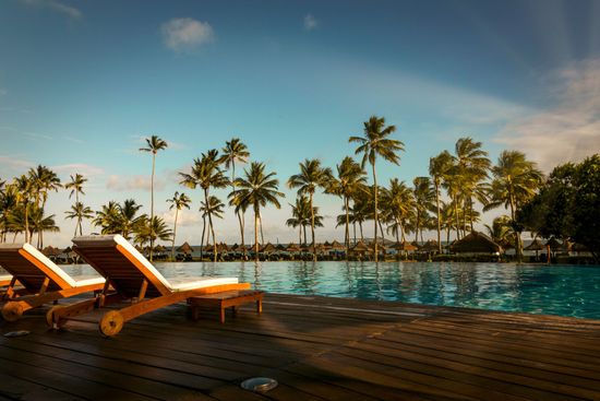 A swimming pool with chairs and palm trees in the background