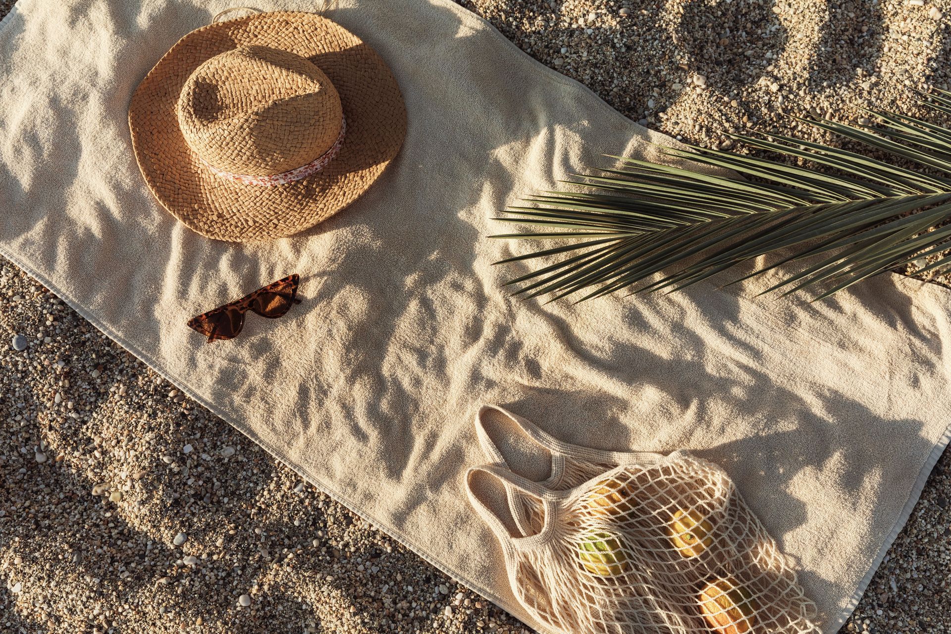 A straw hat , sunglasses , a bag and a palm leaf are on a towel on the beach.