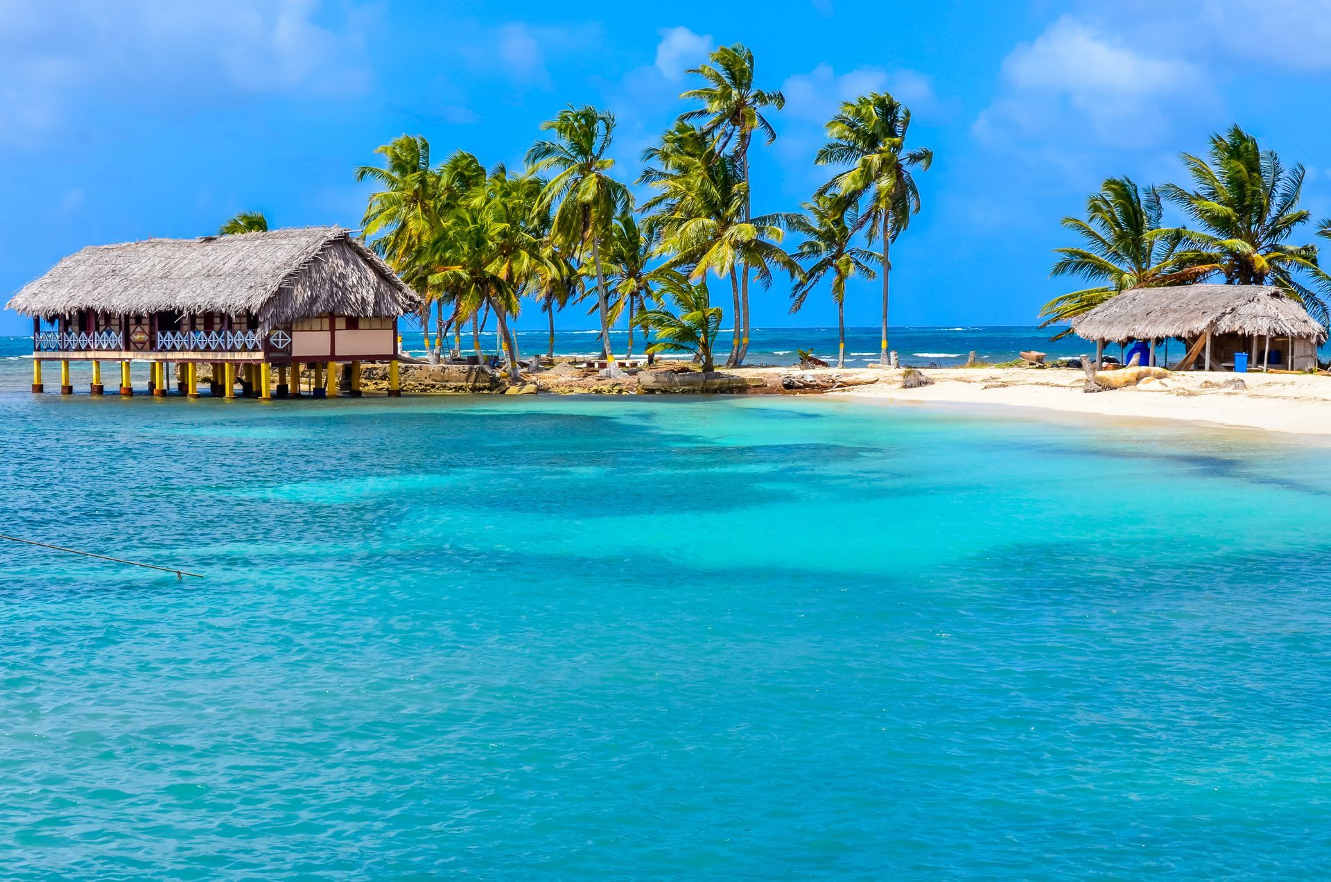 A small island in the middle of the ocean with palm trees and a hut.