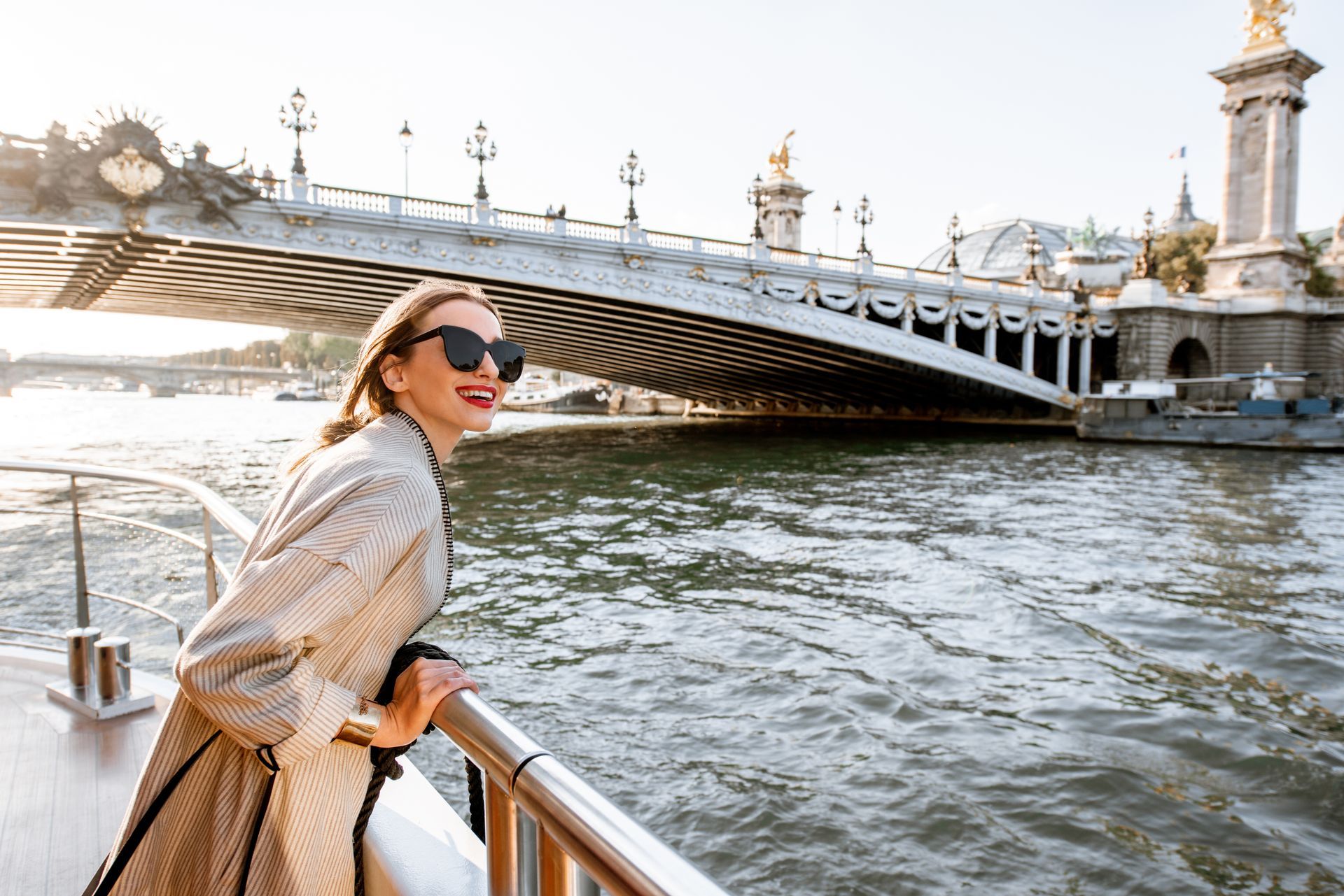 A woman is standing on a boat in front of a bridge over a river.