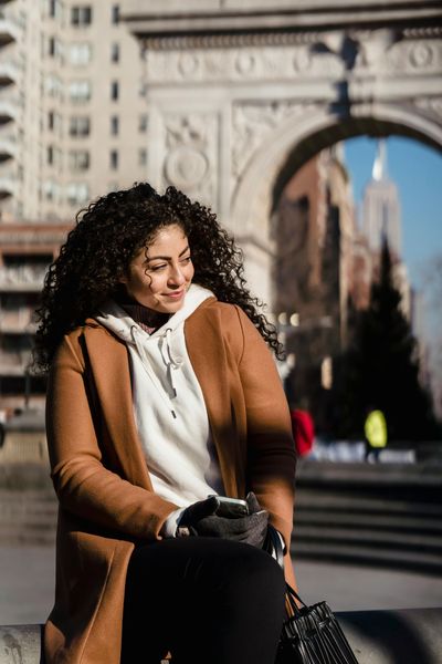 A woman with curly hair is sitting on a sidewalk in front of a building.
