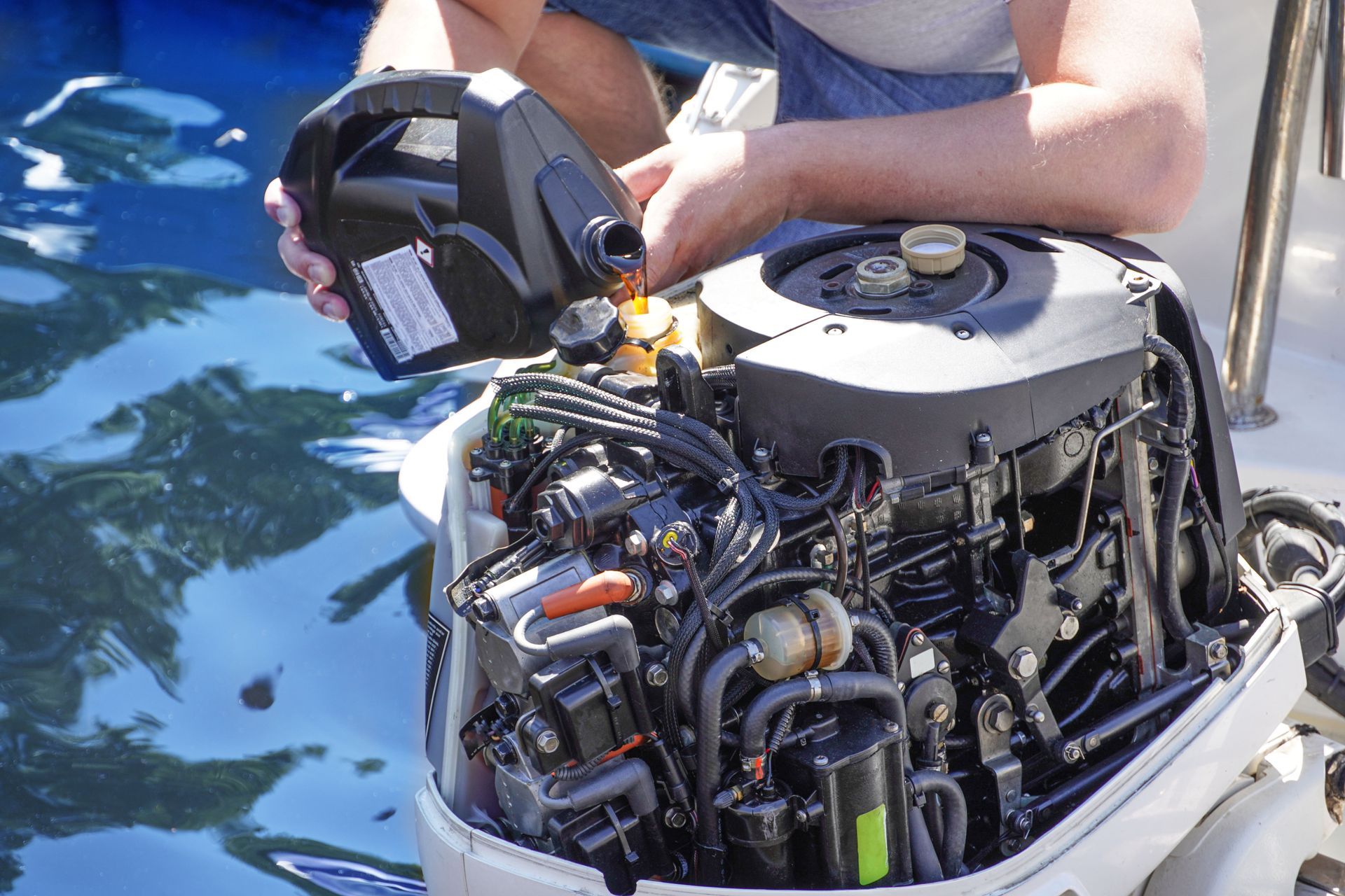 A cropped view of a man pouring and refuelling engine motor oil into the engine of a boat.