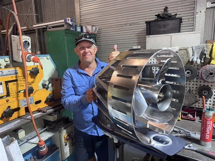 Man in blue shirt holding a large metal industrial drum in a workshop