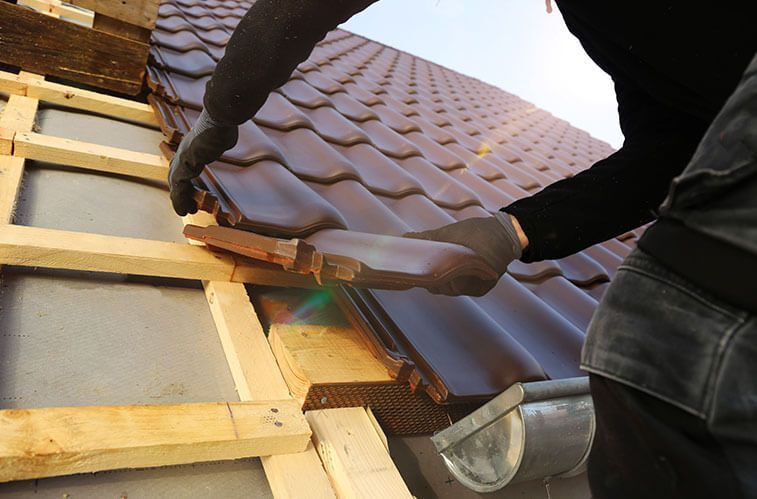 A man is installing a tile roof on a house.