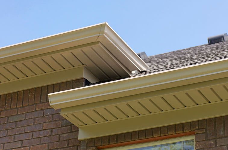 The roof of a brick house with a gutter and a window.