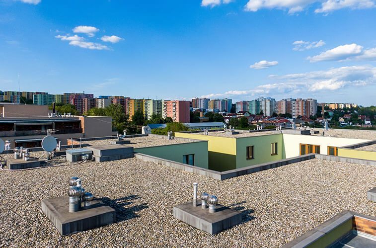 The roof of a building with a gravel roof and a city in the background.