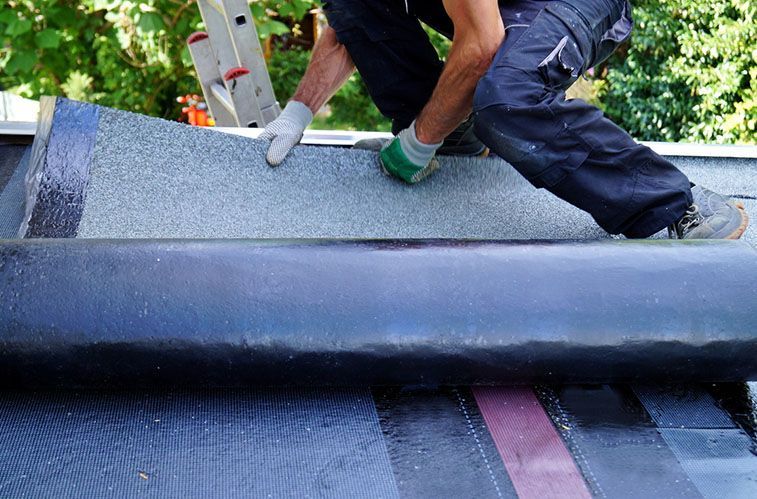 A man is laying a roll of roofing material on top of a roof.