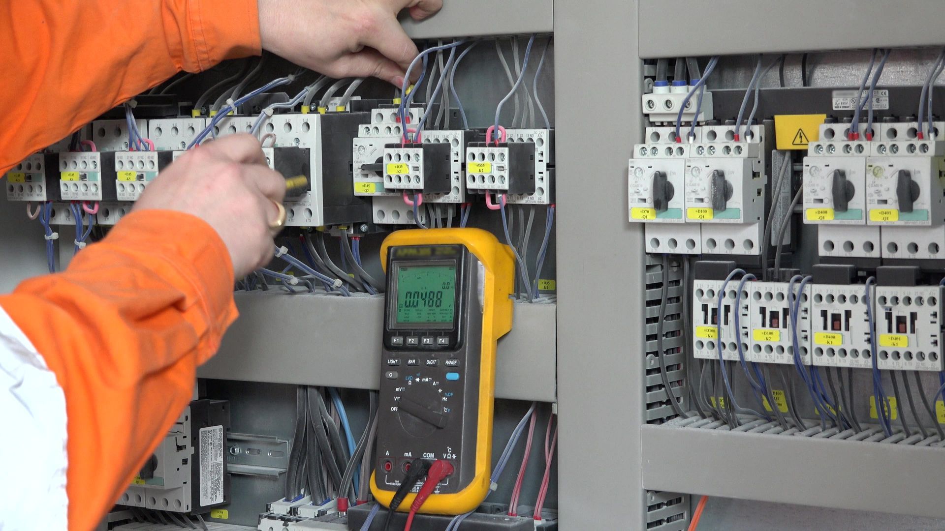 Electrician Using A Multimeter To Test Wires Inside An Electrical Panel, Wearing An Orange Shirt — Townsville Electrical and Appliance Repairs In North Ward, QLD