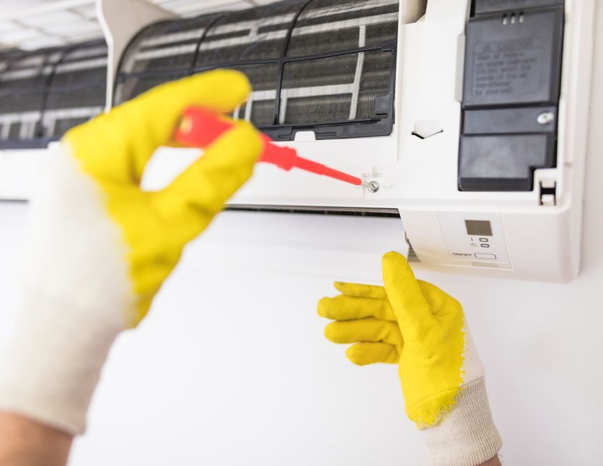 Man Wearing Yellow Gloves Repairing Air Conditioning — Townsville Electrical and Appliance Repairs In Garbutt QLD