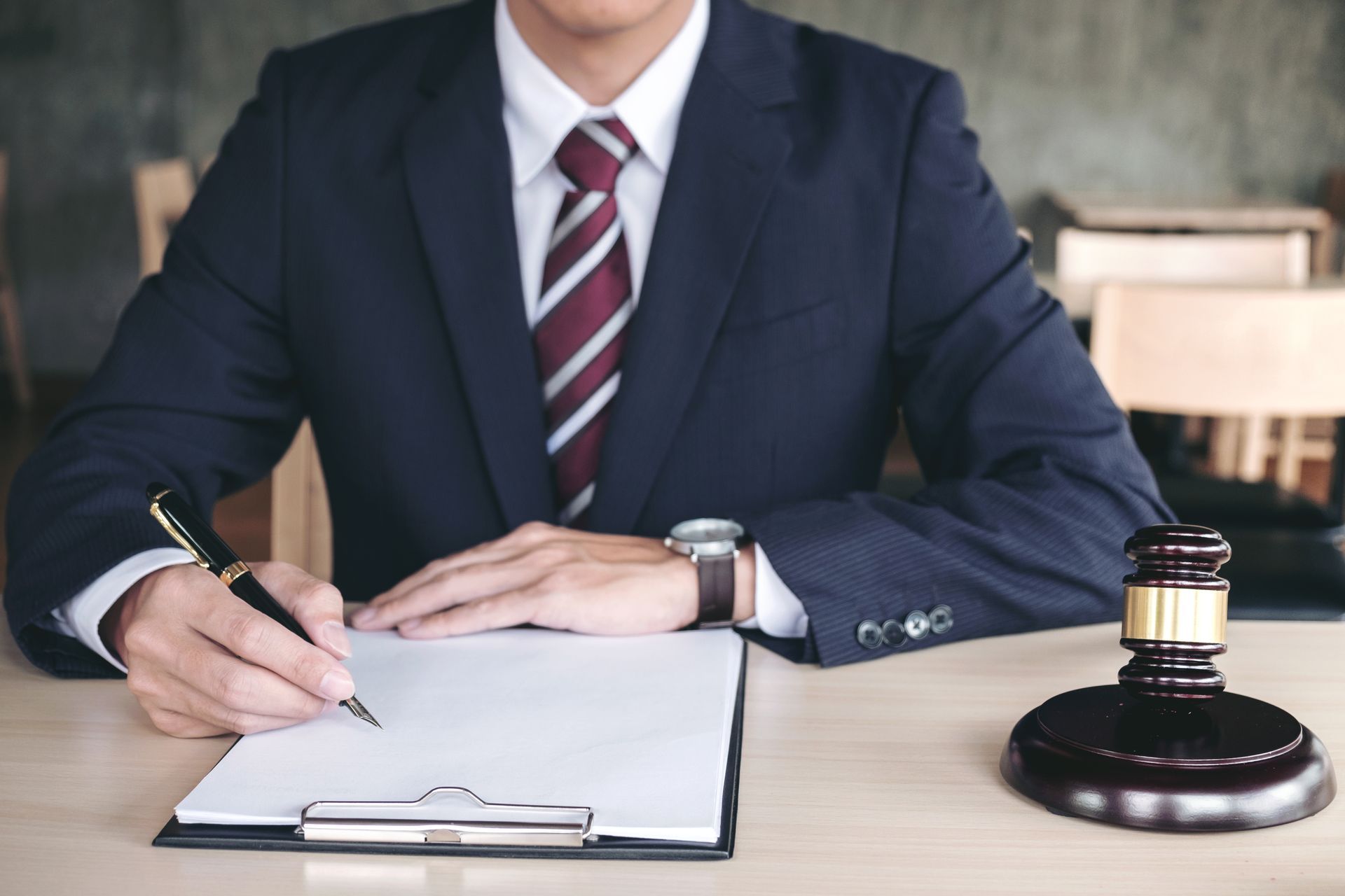 Person in a suit writing on a document at a desk with a gavel.