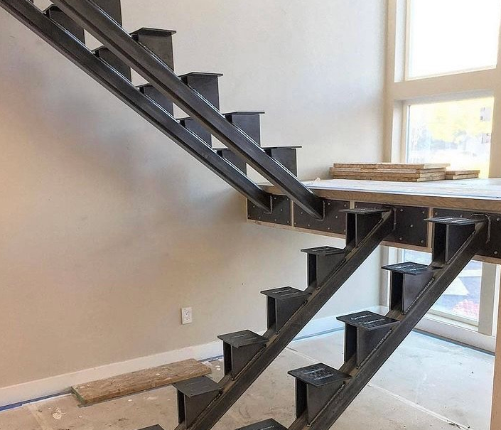 Steel staircase under construction, with open risers and landing, indoors.
