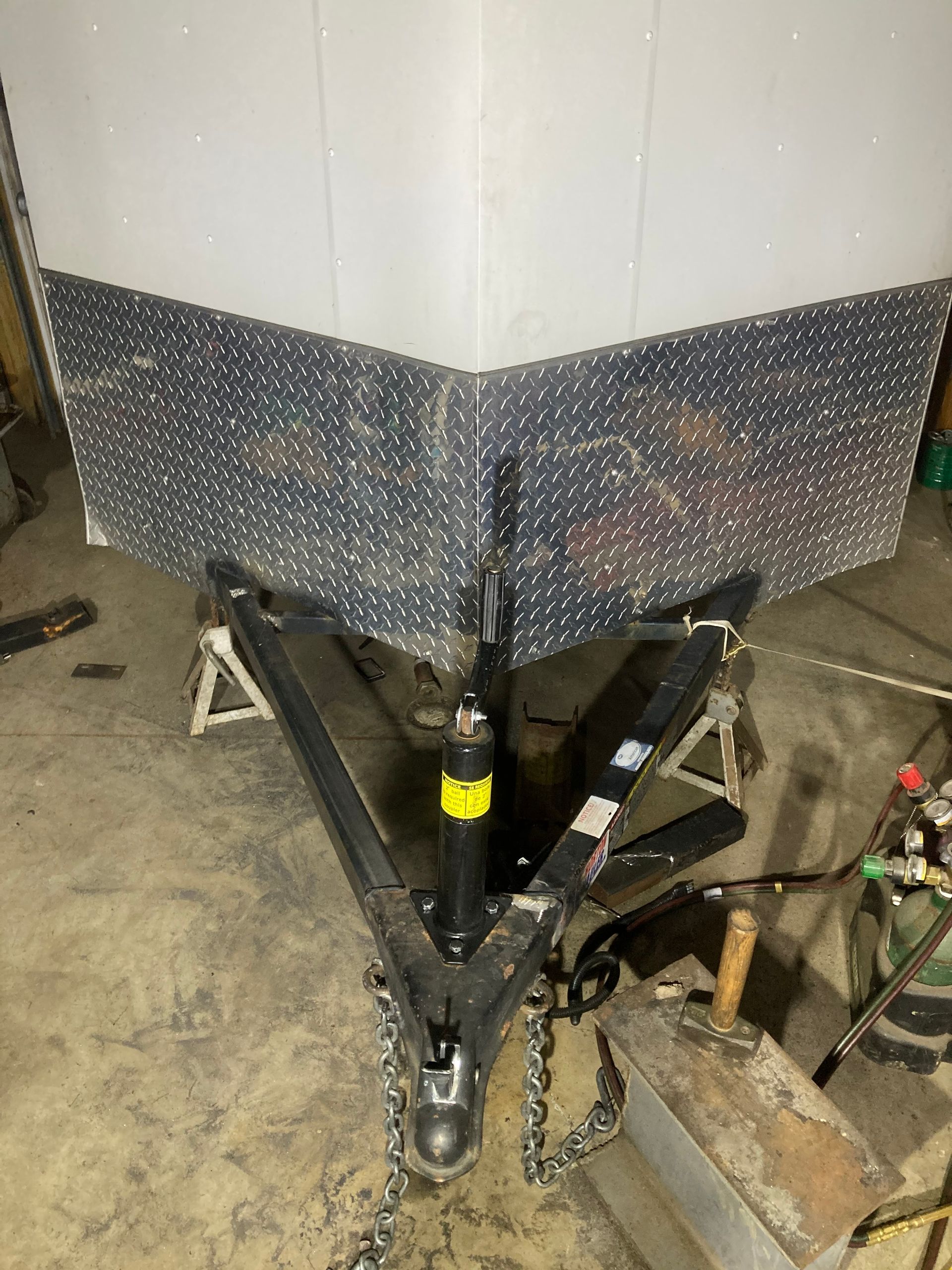 Trailer with diamond-plate panels, supported by jack stands, in a workshop setting.