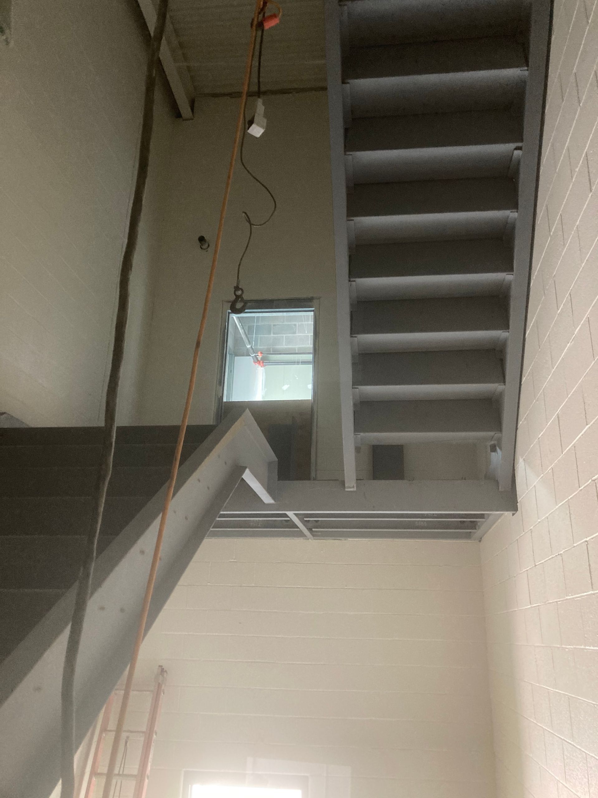 Concrete stairs in a building under construction. Staircase leads up and down, with an electrical cord hanging down.