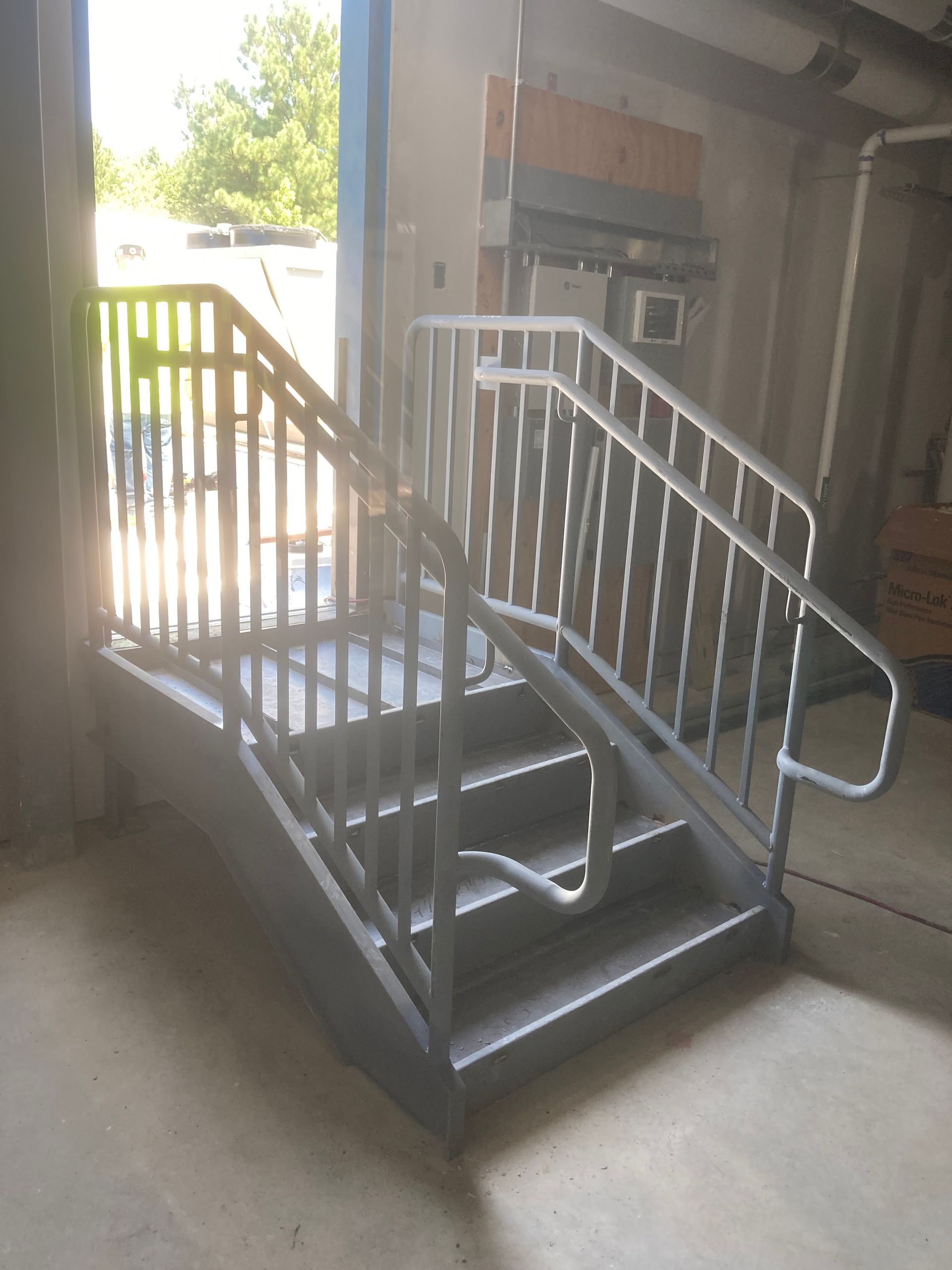 Metal staircase with handrails, leading to a doorway. Indoors, natural light.
