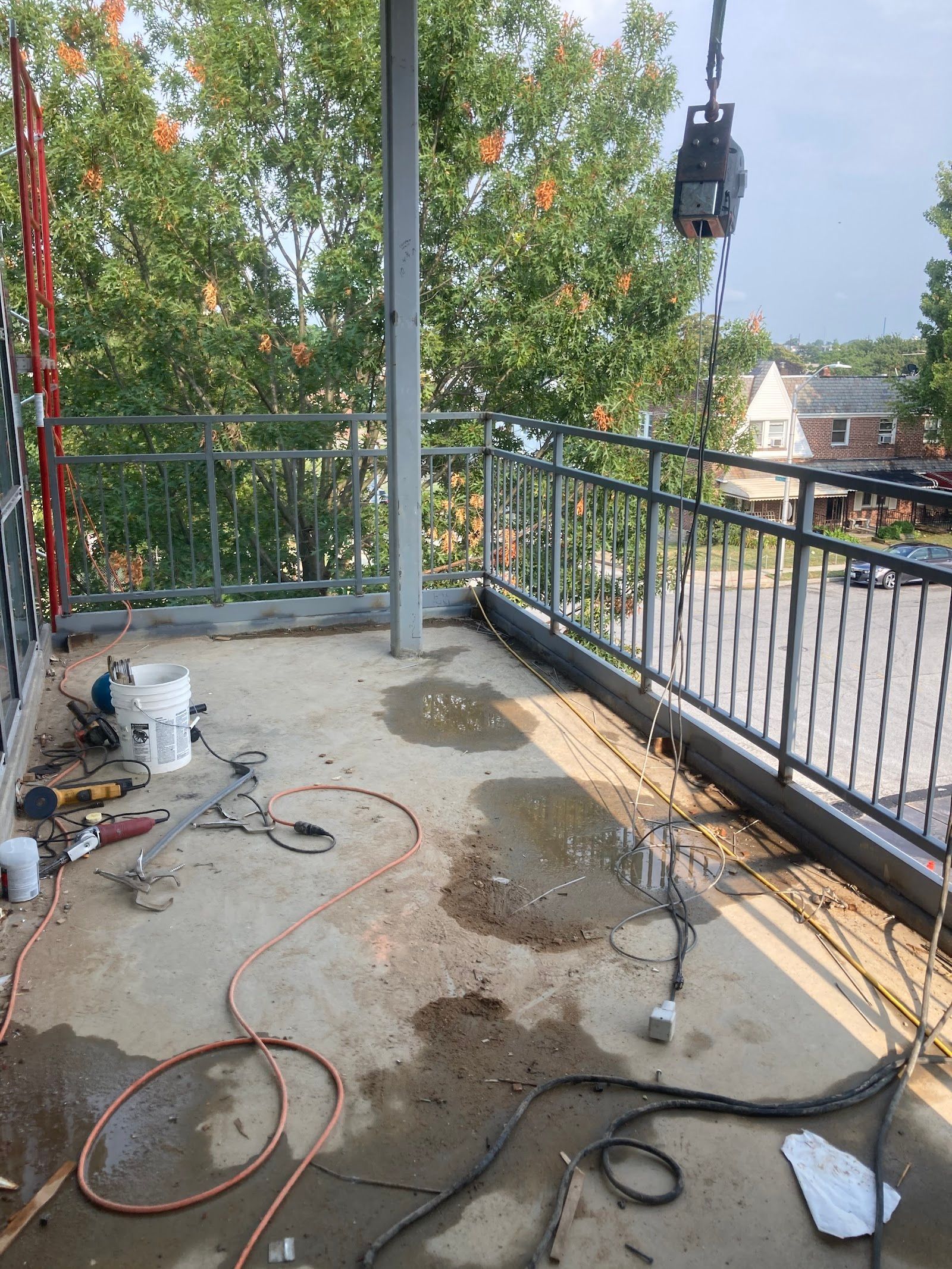 Construction site on a concrete patio. Tools and water are scattered about, metal railings and support beams.