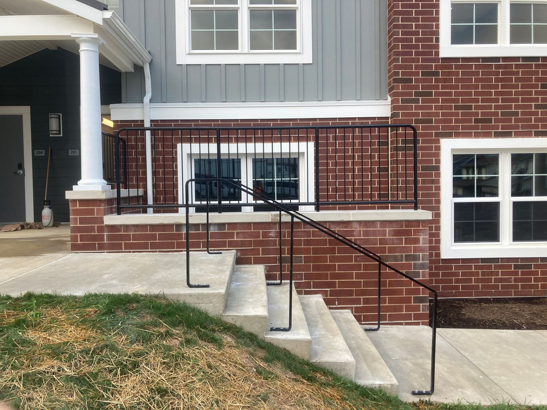 Exterior view of a building with brick and gray siding, concrete steps, and a black metal railing.