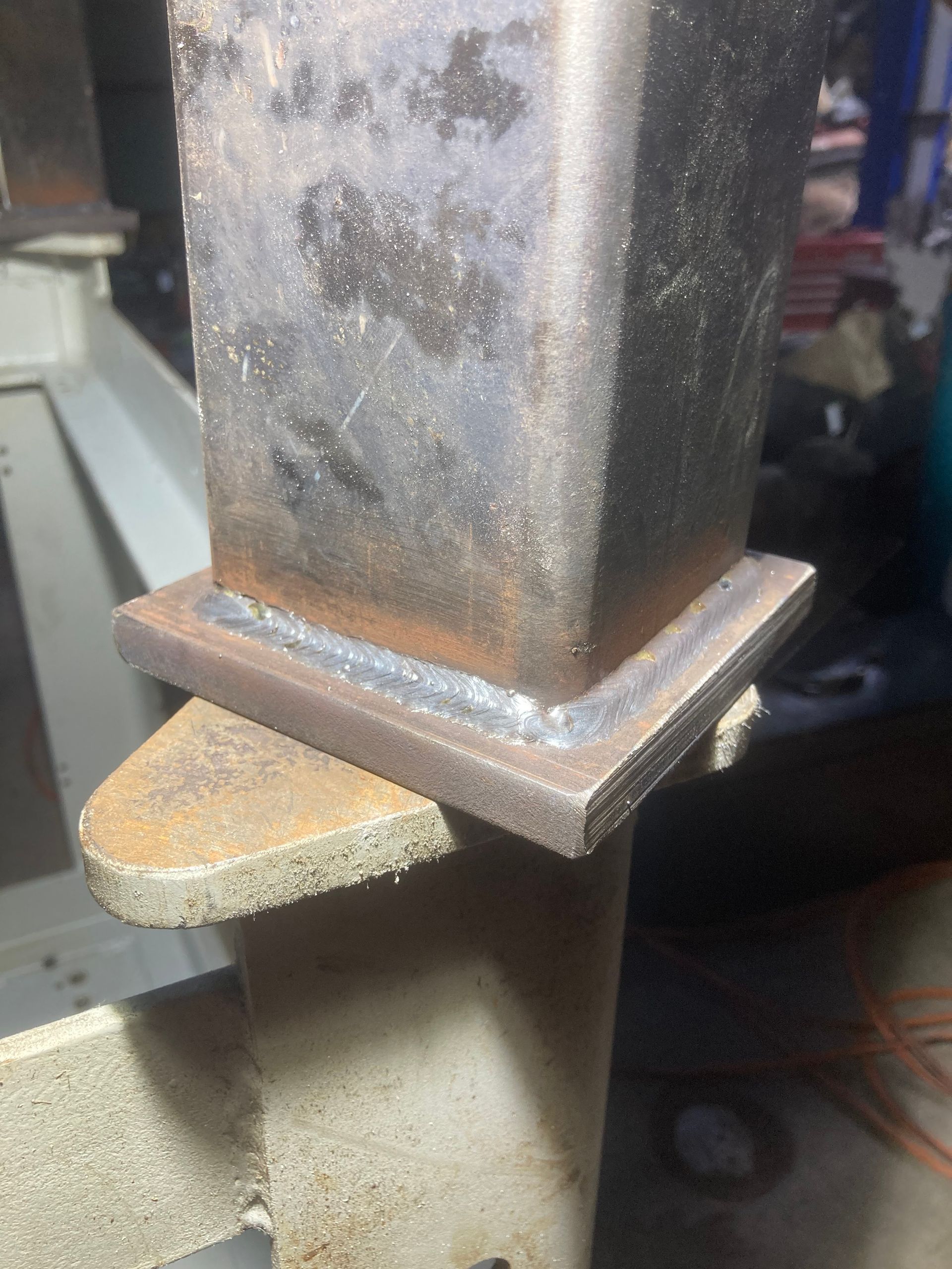 Close-up of a welded metal post to a base plate, in a workshop setting.