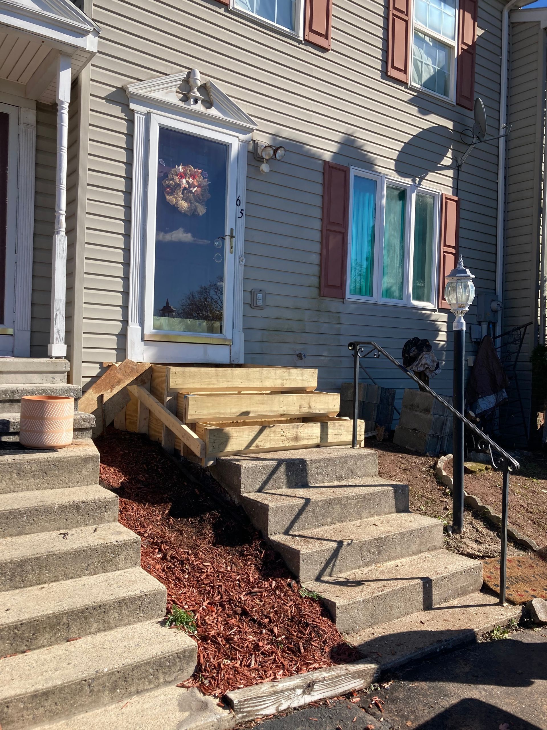 Gray house with concrete stairs, new wooden steps, and red mulch along the side.