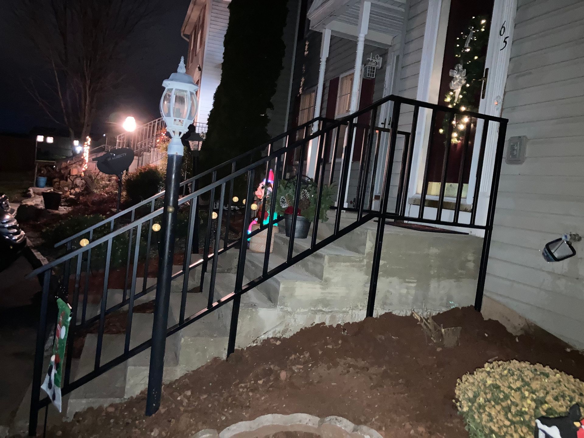 Black metal handrails on concrete steps leading to a house entrance. Night scene, some Christmas decorations.
