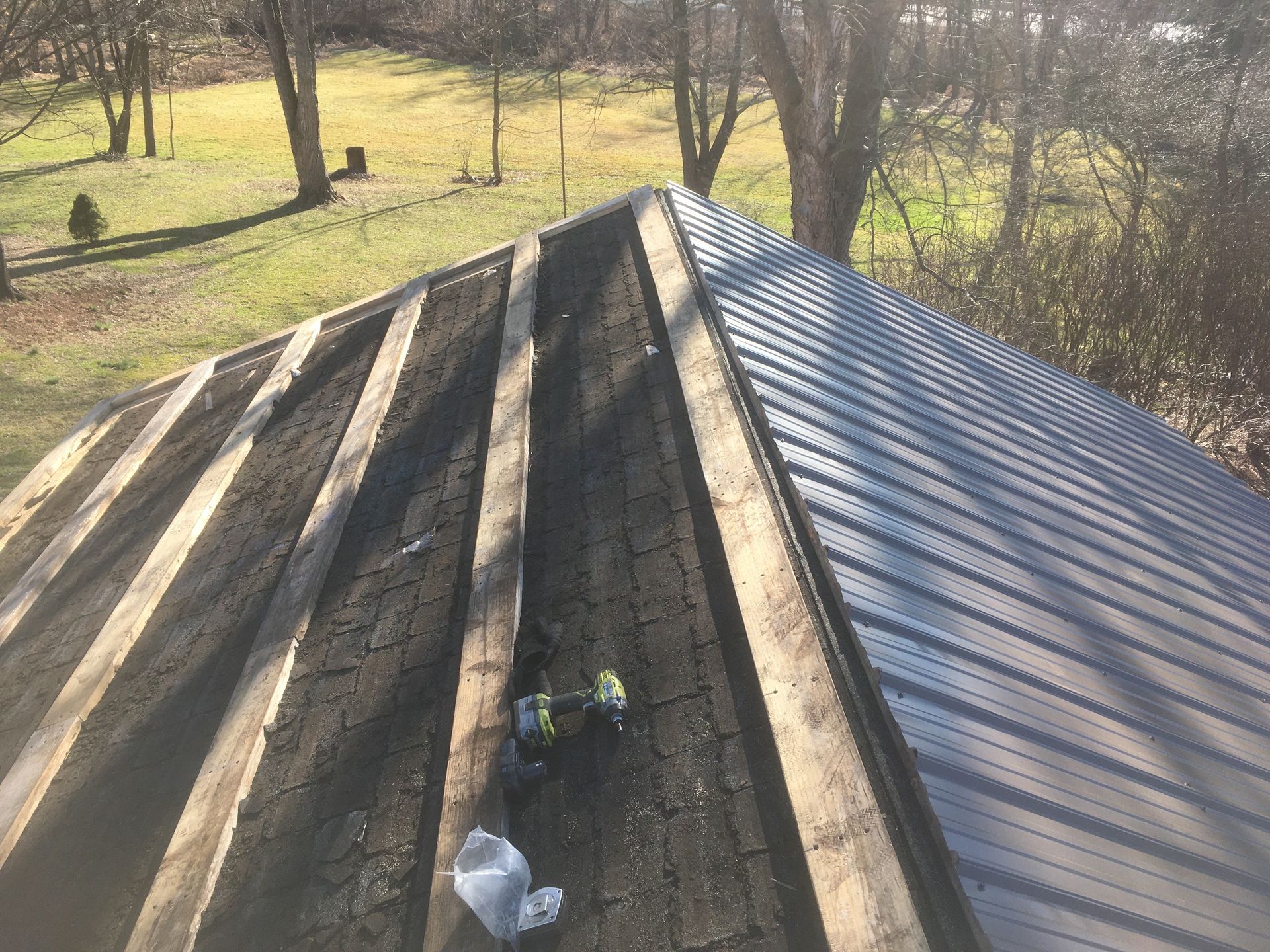 Roof with metal panels being installed, exposed wooden rafters and tools visible. Outdoor setting.