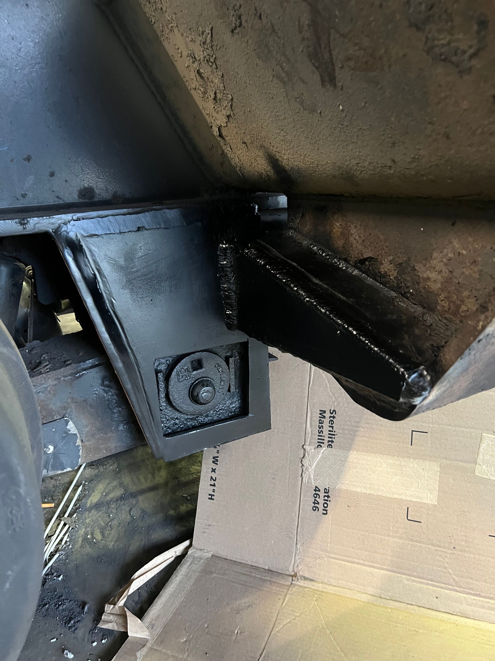 Black painted metal frame and support structure attached to a vehicle's underside, with a bolt visible.