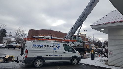 A white van is parked in front of a building with a crane attached to it.