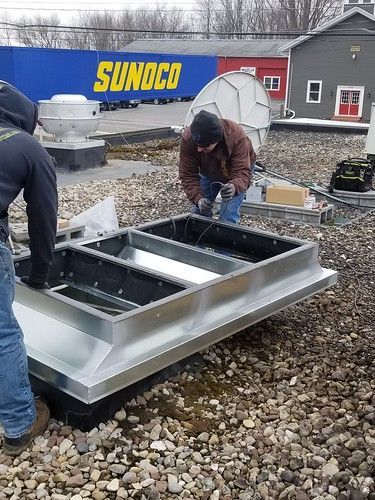 Two men are working on a metal structure on the roof of a building.