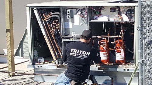 A man wearing a triton shirt is working on a machine.