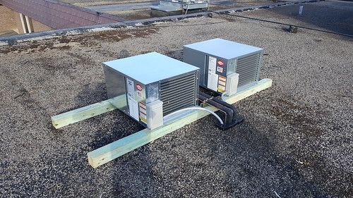 Two air conditioners are sitting on top of a gravel roof.
