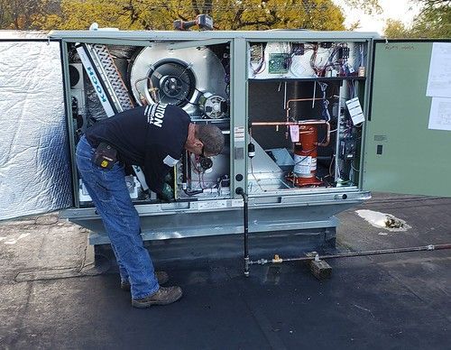 A man is working on an air conditioner on a roof