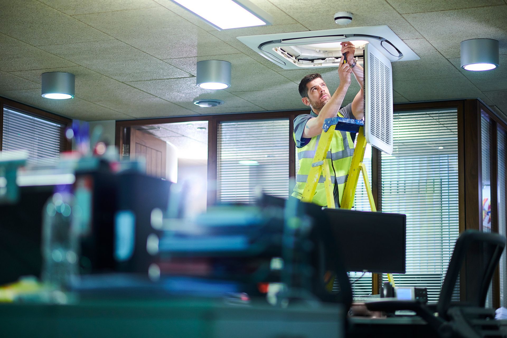 A man is working on a ceiling fan in an office.