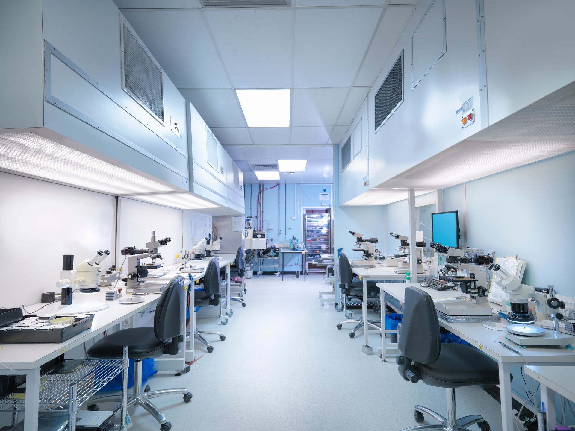 A laboratory with a lot of tables and chairs and microscopes.