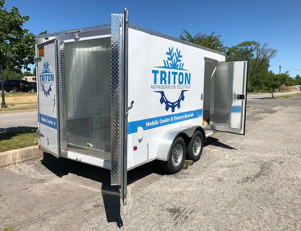 A triton trailer is parked in a parking lot with its doors open.