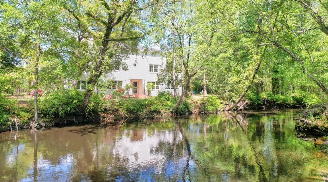 A house is reflected in the water of a pond surrounded by trees.