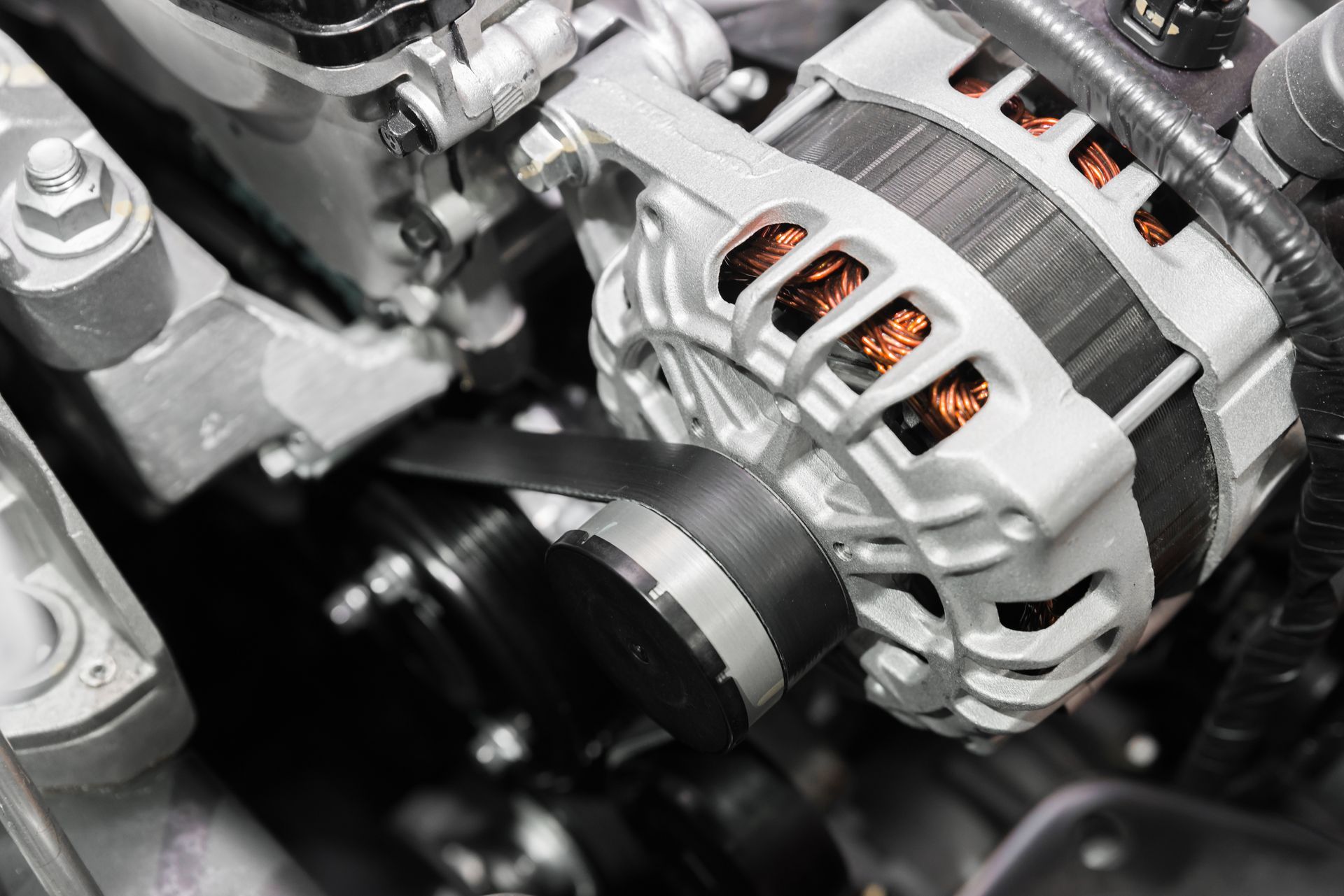 Close-up of a car alternator, with a black belt wrapped around a pulley, attached to the engine. | Cars Land Service Center LLC