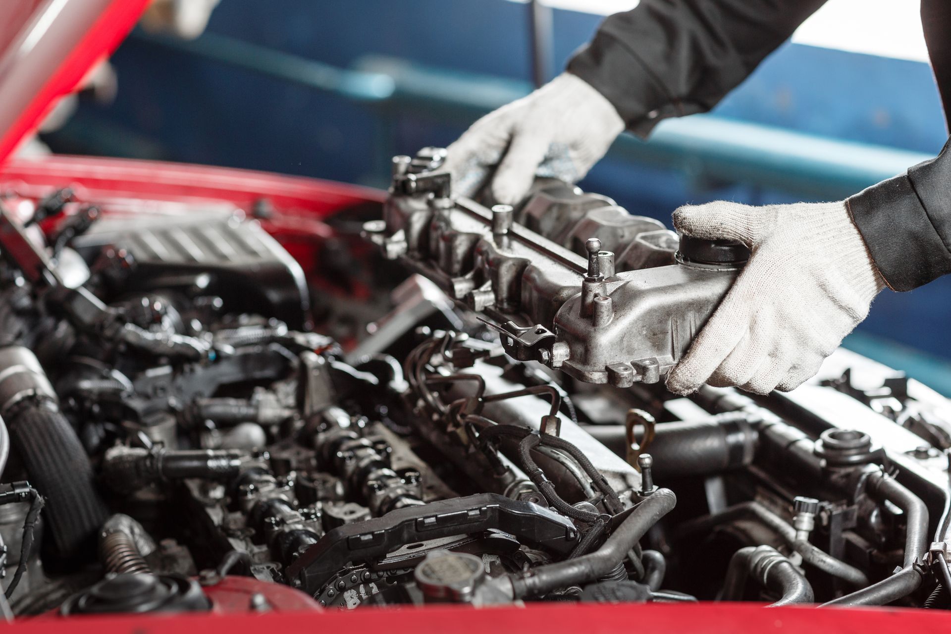 Mechanic removing a car engine component with gloved hands in a red vehicle. | Cars Land Service Center LLC