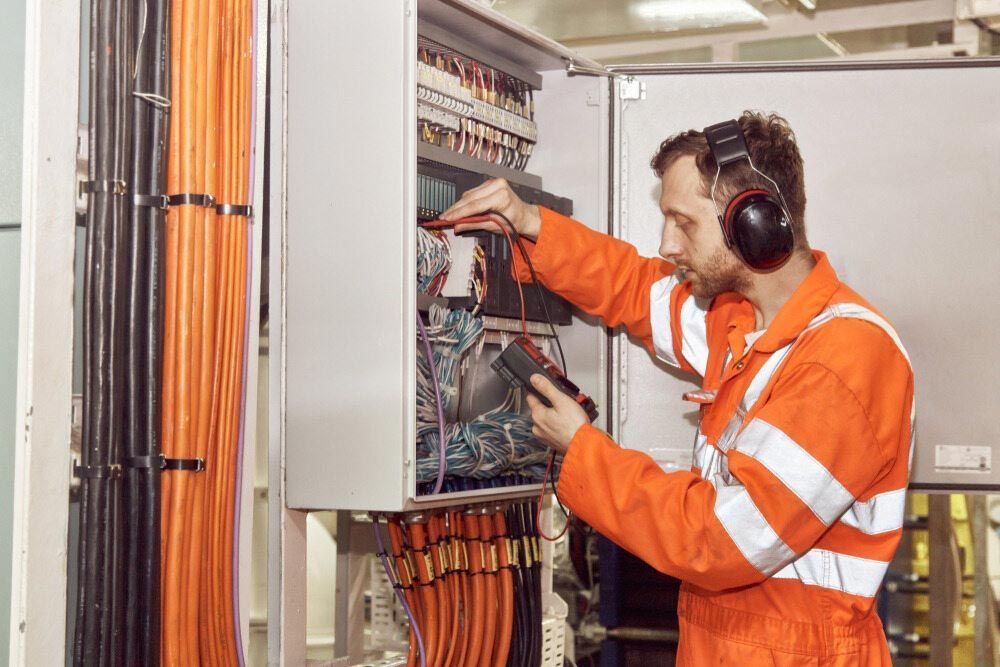 A Man Wearing Headphones Is Working On An Electrical Box — EESI Electrical Contractors In Alstonville, NSW
