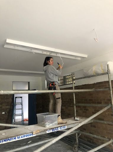 A Man Is Hanging A Light Fixture From The Ceiling — EESI Electrical Contractors In Alstonville, NSW