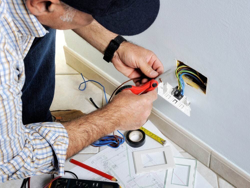 A Man Is Working On An Electrical Outlet On A Wall — EESI Electrical Contractors In Alstonville, NSW