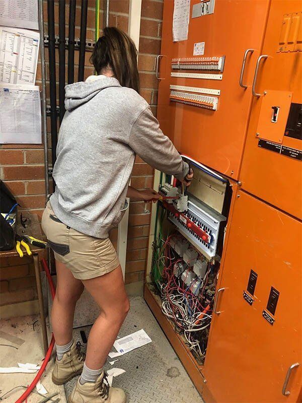 A Woman Is Working On An Electrical Box In A Room — EESI Electrical Contractors In Alstonville, NSW