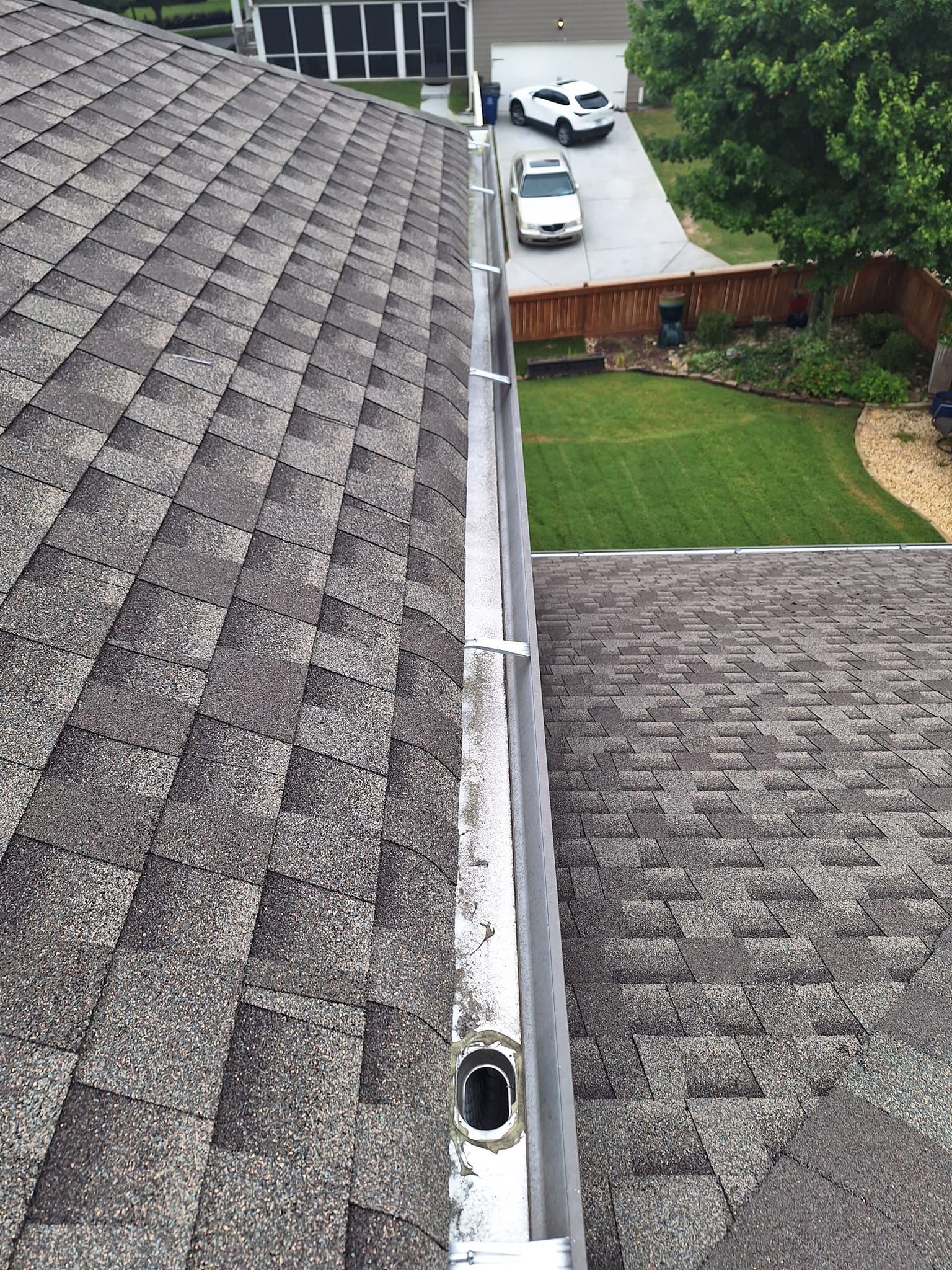 A gutter on the roof of a house with cars parked in the driveway.