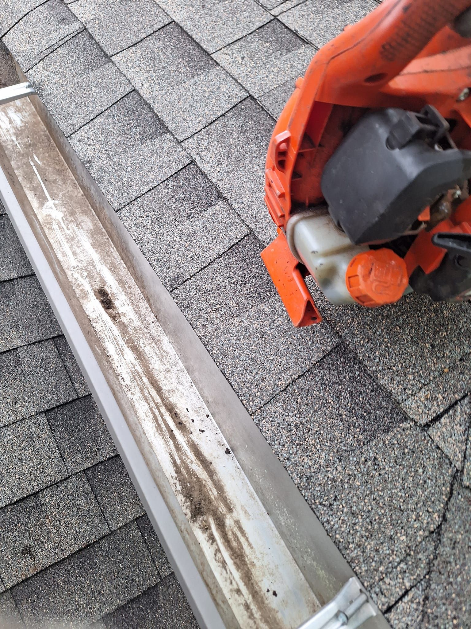 A lawn mower is sitting on top of a roof next to a gutter.