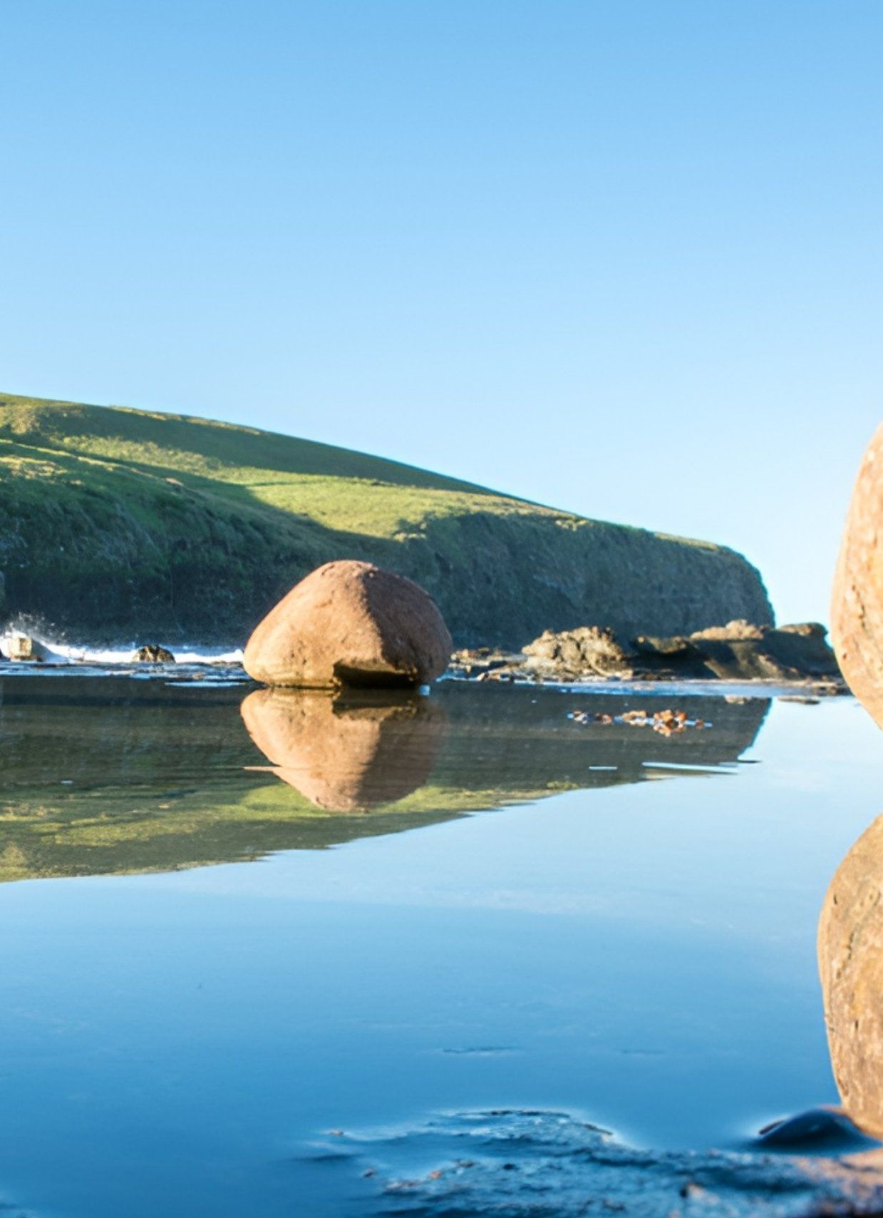 Three Large Rocks Reflected In Water With Green Hillside — JSF Interiors Goulburn in Kiama, NSW