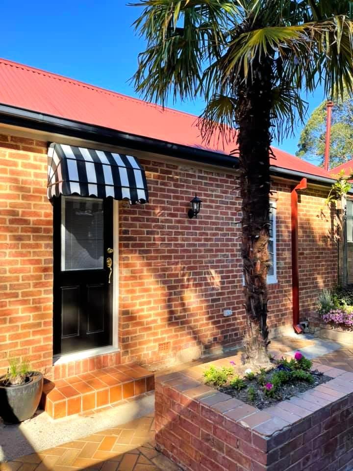 Brick House With Black Door And Striped Awning — JSF Interiors Goulburn in Albion Park, NSW