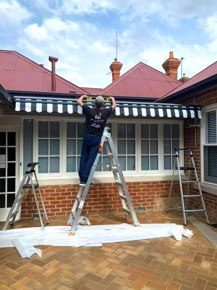 Installing Striped Awning On Brick Building — JSF Interiors Goulburn in Albion Park, NSW