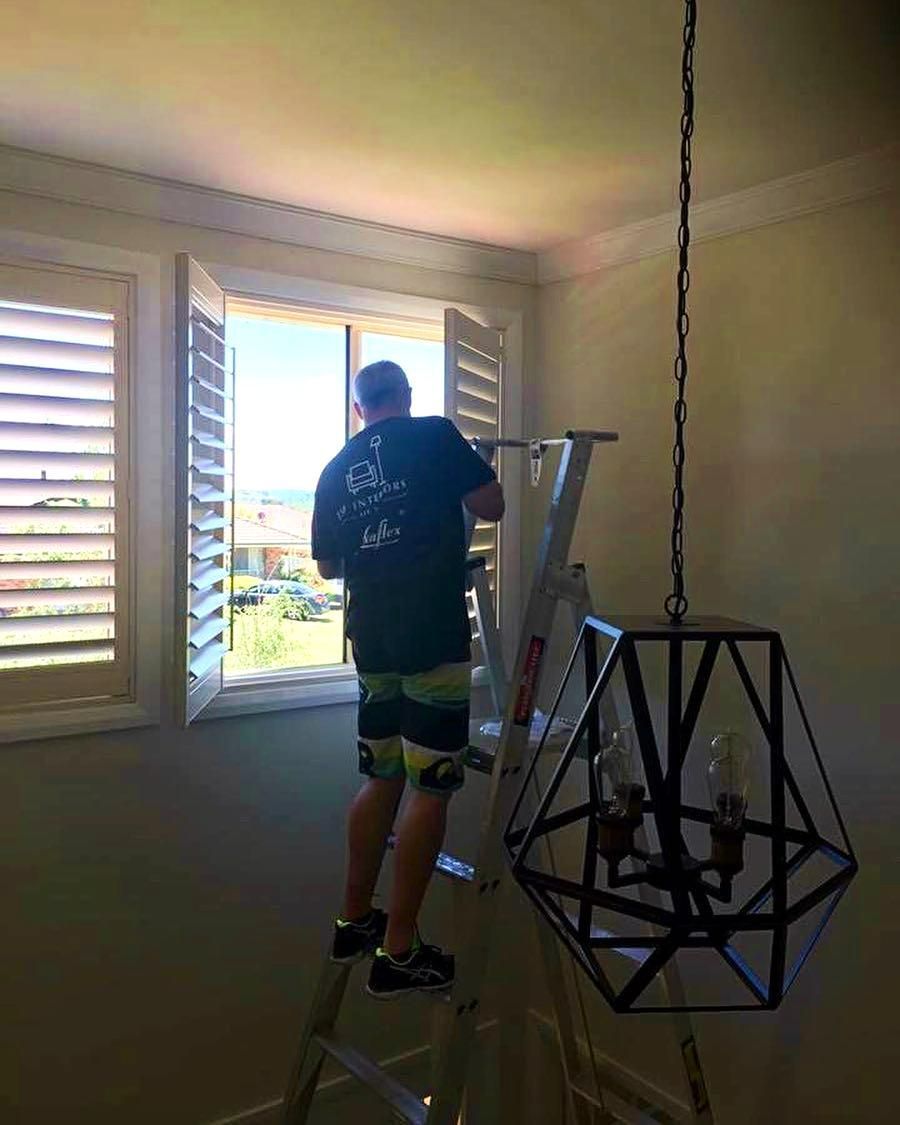 Man Adjusting Window Shutters With Hanging Light — JSF Interiors Goulburn in Berry, NSW