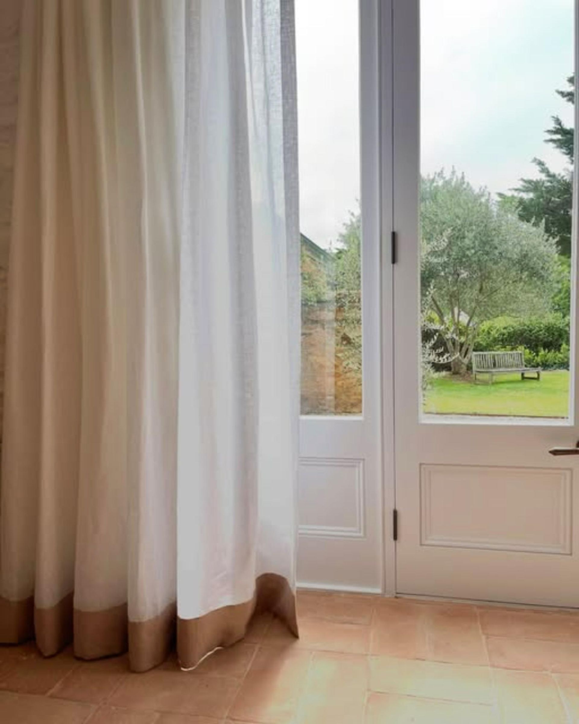 White Curtain With Brown Border Next To Door Overlooking Green Yard — JSF Interiors Goulburn in Goulburn, NSW