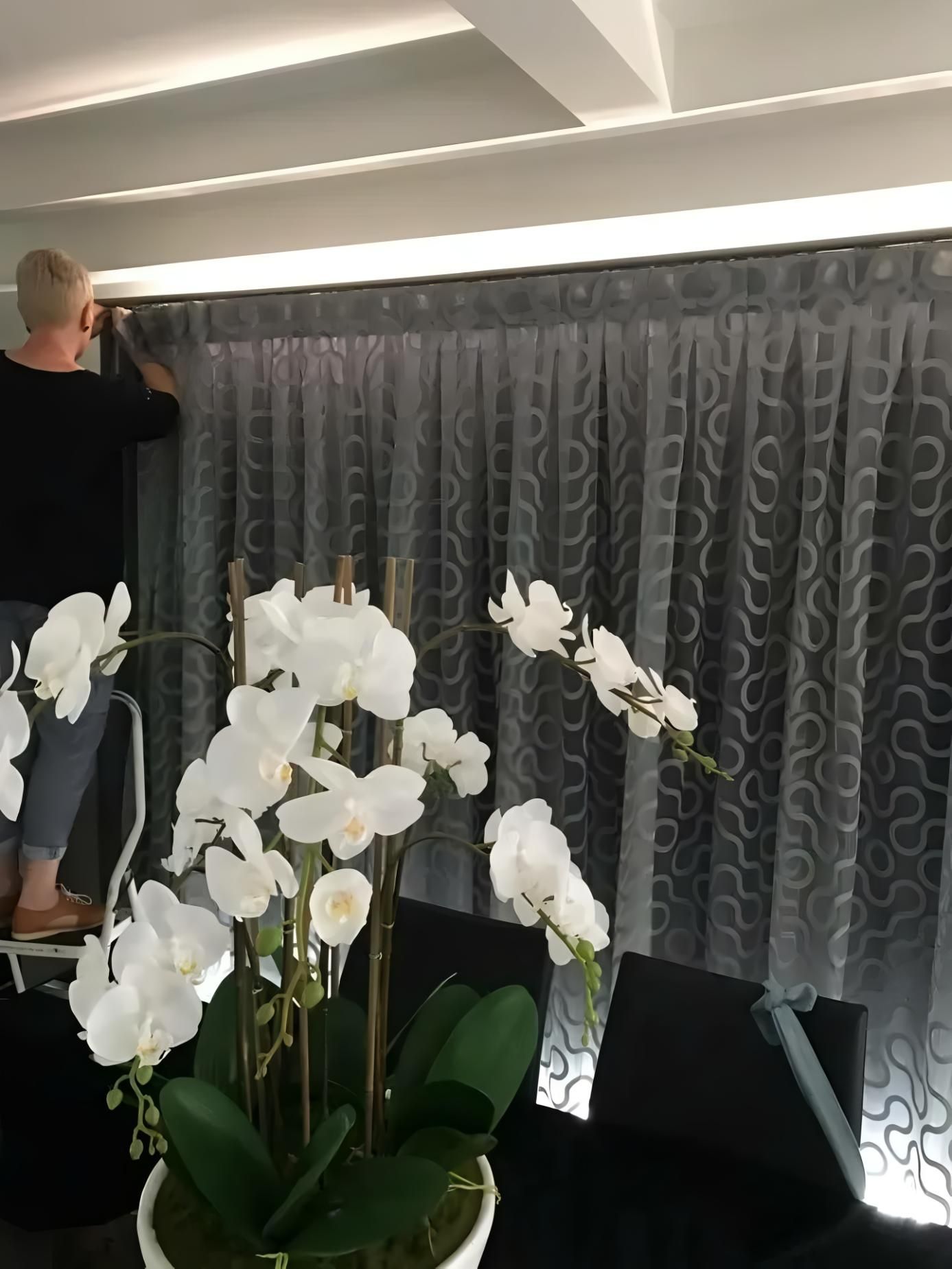 Person On Ladder Adjusting Gray Patterned Curtains — JSF Interiors Goulburn in Goulburn, NSW