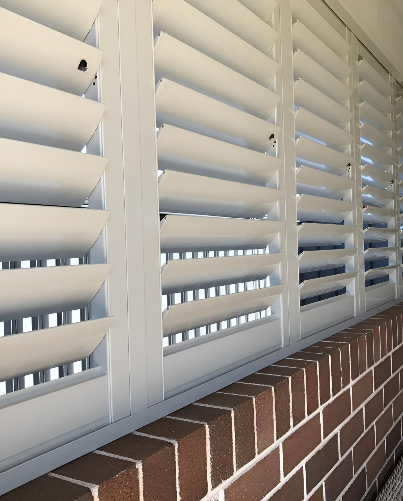 White Shutter Blinds Along a Brick Wall, Partially Open to Let in Light — JSF Interiors Goulburn in Moss Vale, NSW